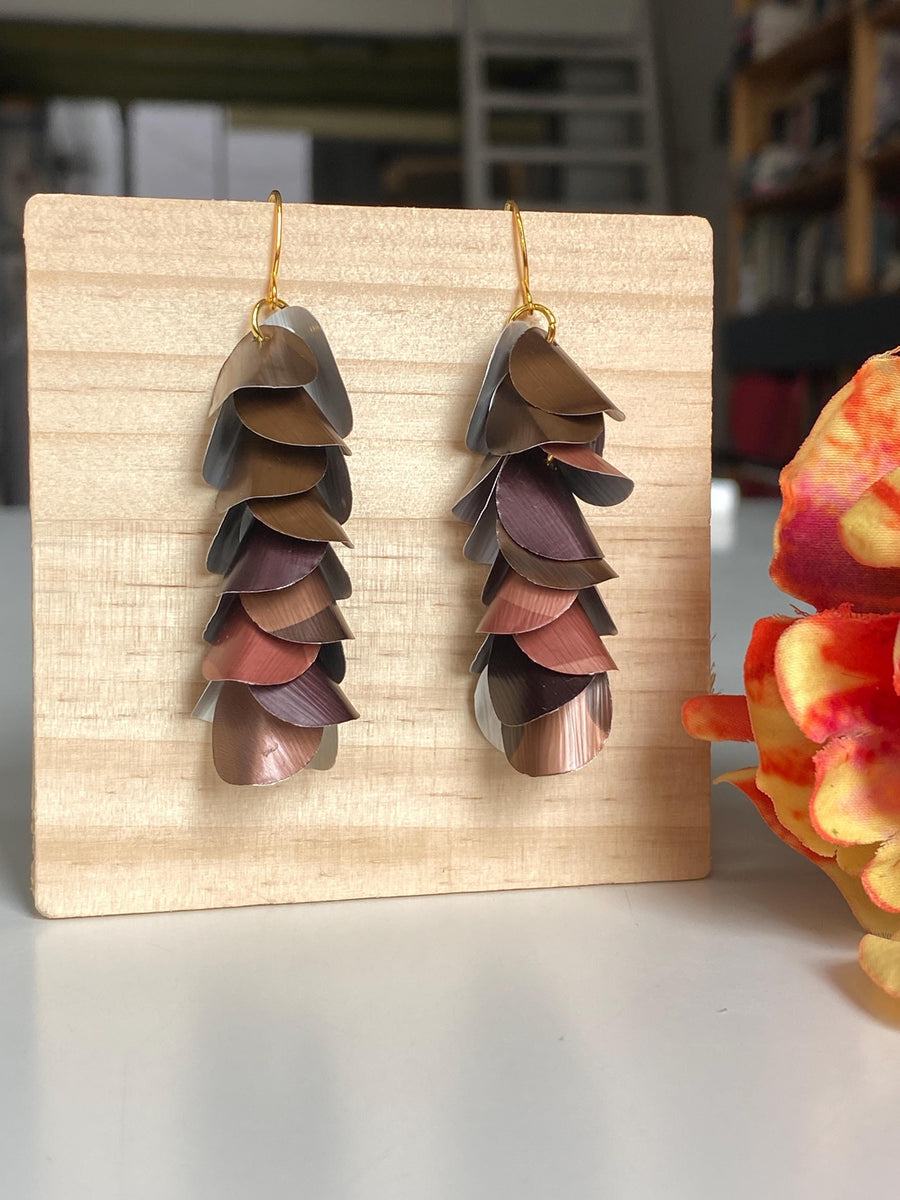 brown coloured cascade earrings made from upcycled nespresso capsules by Laura Zabo, on a wooden background a flower decoration