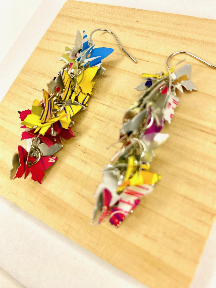 colourful cascade earrings featuring tiny butterfly layers made from upcycled craft beer cans by laura zabo, on a wooden and white background