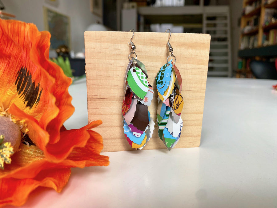 colourful cascade earrings made from craft beer and soda cans by laura zabo on a wooden background and flower decoration