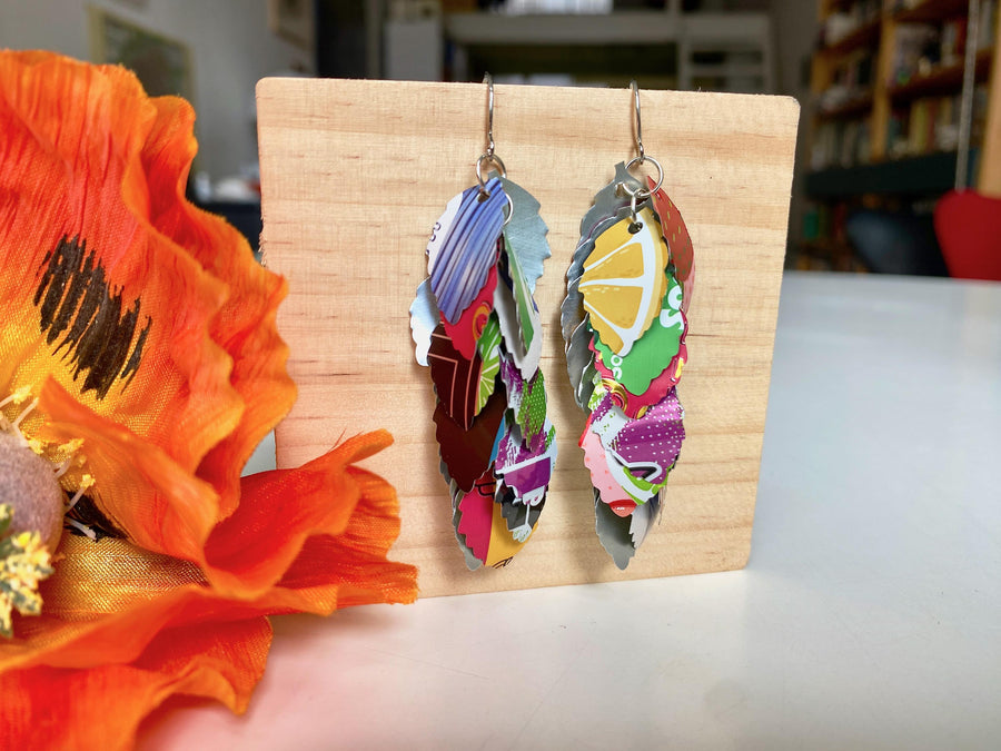 colourful cascade earrings made from craft beer and soda cans by laura zabo on a wooden background and flower decoration