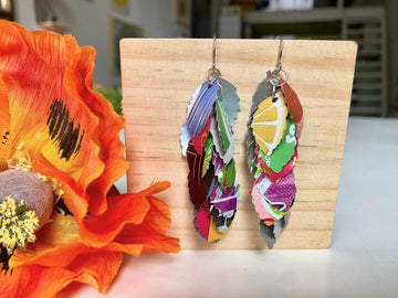 colourful cascade earrings made from craft beer and soda cans by laura zabo on a wooden background and flower decoration
