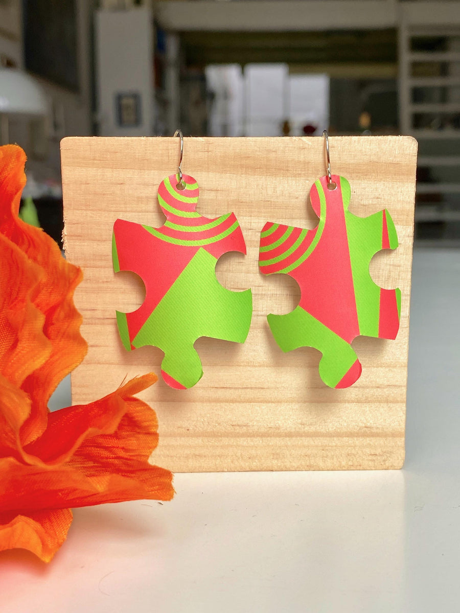 puzzle shaped earrings in bright green and peach colour made from upcycled craft beer can by laura zabo on a wooden background and flower decoration