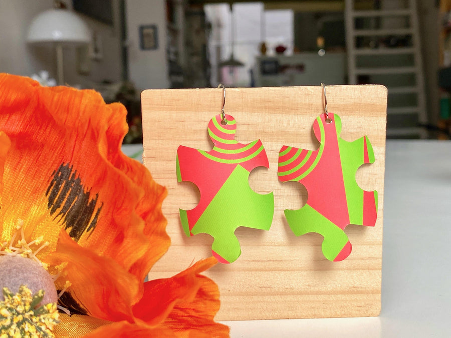 puzzle shaped earrings in bright green and peach colour made from upcycled craft beer can by laura zabo on a wooden background and flower decoration