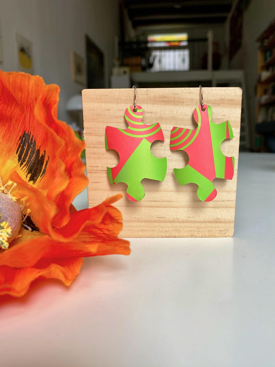 puzzle shaped earrings in bright green and peach colour made from upcycled craft beer can by laura zabo on a wooden background and flower decoration