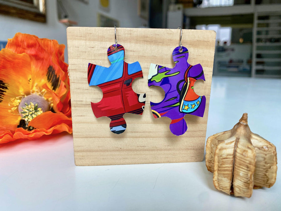 blue purple red graffiti, urban style puzzle shaped earrings made from upcycled beer can by laura zabo on a wooden background and flower decoration
