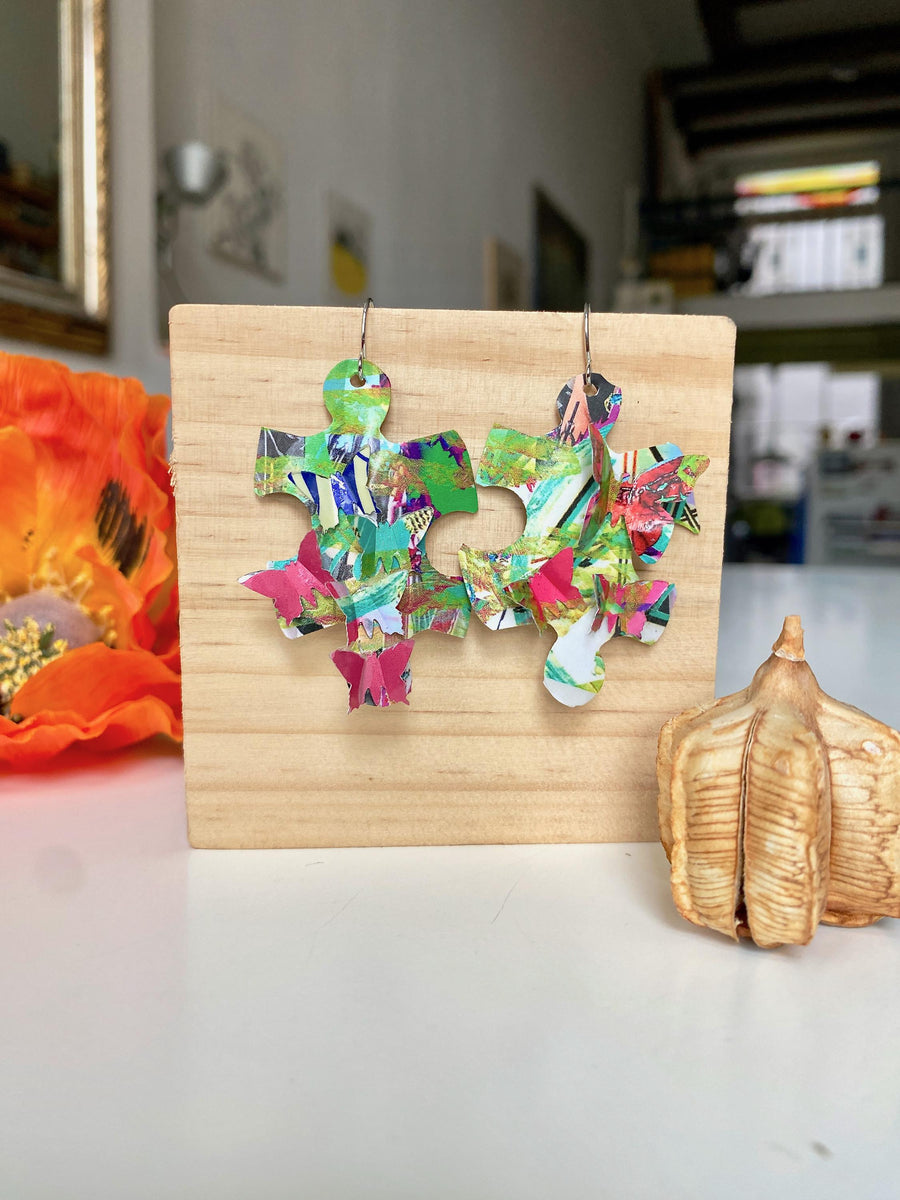 colourful, puzzle shaped earrings adorned with tiny butterflies made from upcycled craft beer cans by laura zabo on a wooden background and flower design