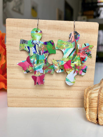 colourful, puzzle shaped earrings adorned with tiny butterflies made from upcycled craft beer cans by laura zabo on a wooden background and flower design