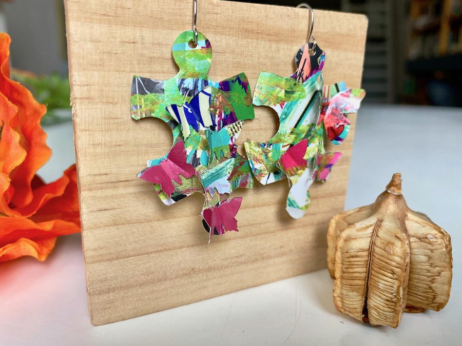 colourful, puzzle shaped earrings adorned with tiny butterflies made from upcycled craft beer cans by laura zabo on a wooden background and flower design
