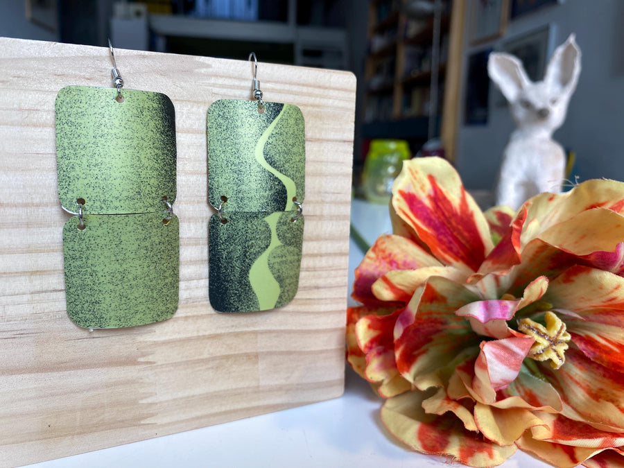mint green and black retro 90s earrings made from upcycled craft beer can by Laura zabo, on a wooden background and flower decoration