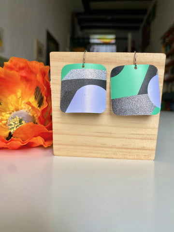 grey green coloured squared geometric earrings made from upcycled craft beer cans by laura zabo on a wooden background and flower