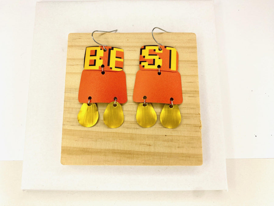 Laura Zabo statement earrings in orange yellow and gold colours, made from upcycled craft beer cans and nespresso capsules on a wooden and white background