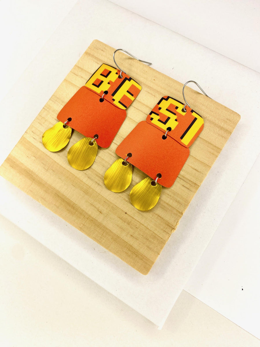 Laura Zabo statement earrings in orange yellow and gold colours, made from upcycled craft beer cans and nespresso capsules on a wooden and white background