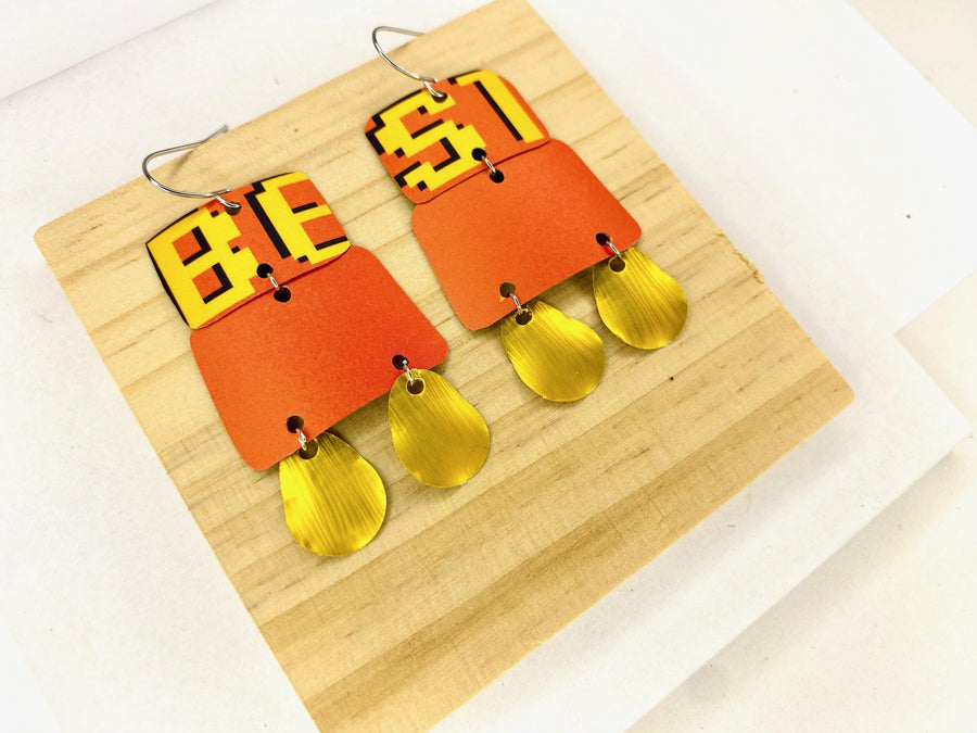 Laura Zabo statement earrings in orange yellow and gold colours, made from upcycled craft beer cans and nespresso capsules on a wooden and white background