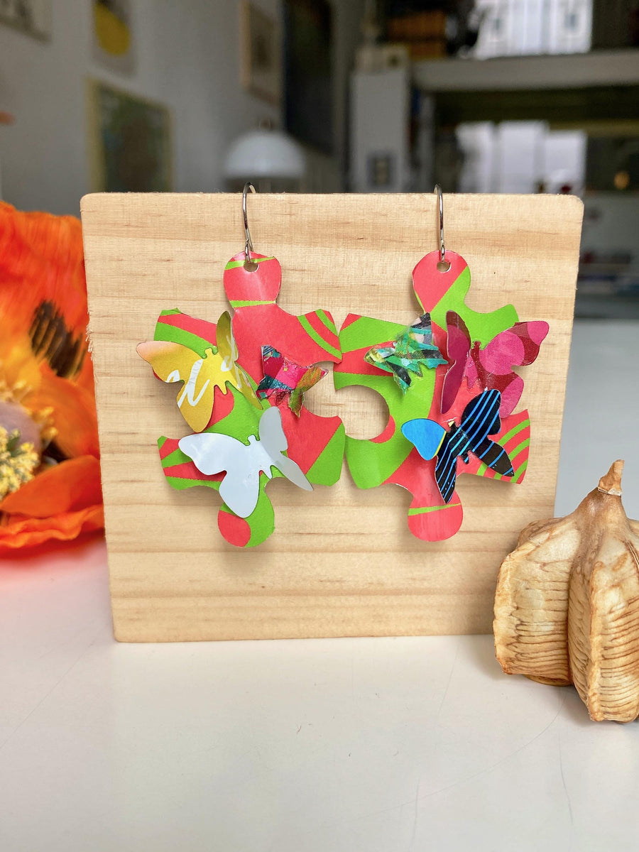 Beautiful, bright, multicoloured, puzzle shaped earrings with tiny butterflies, made from upcycled craft beer cans by Laura Zabo on a wooden background