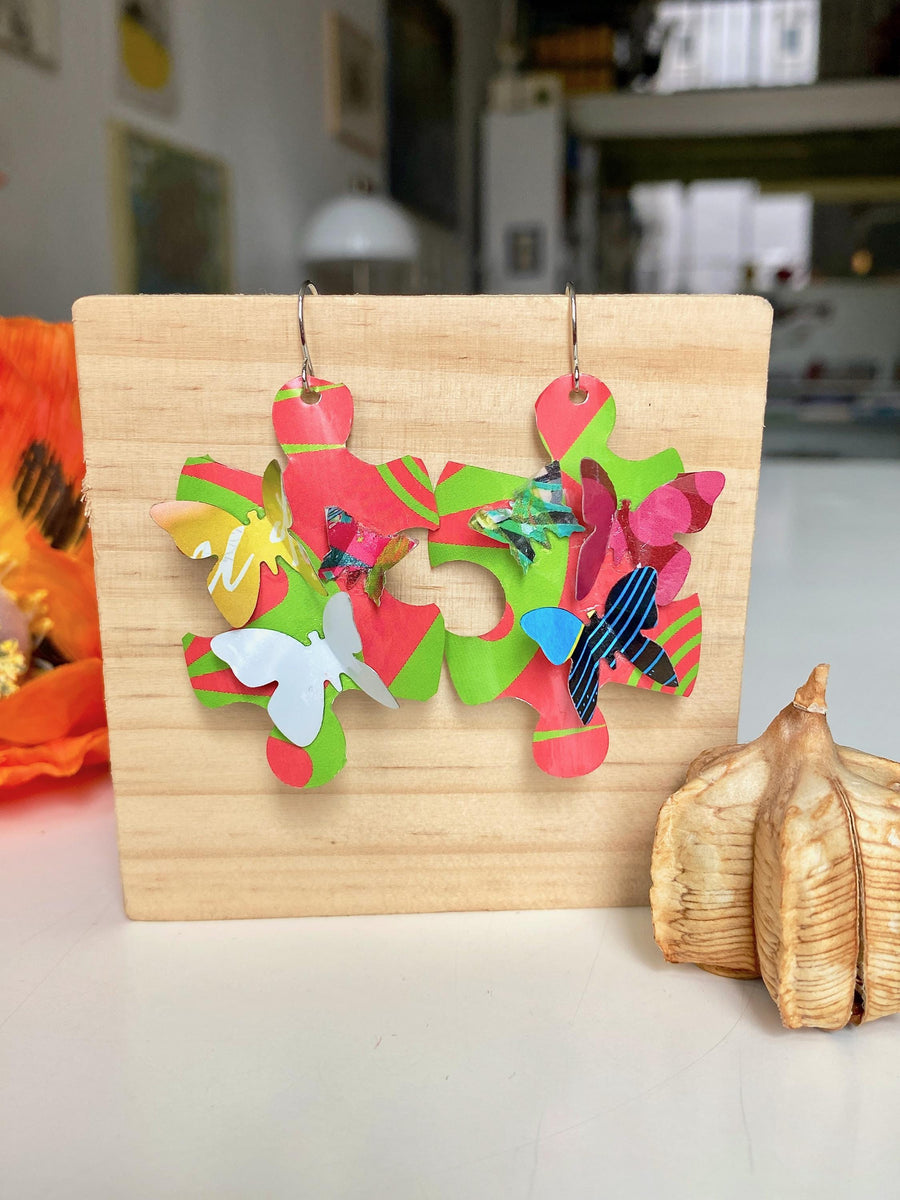 Beautiful, bright, multicoloured, puzzle shaped earrings with tiny butterflies, made from upcycled craft beer cans by Laura Zabo on a wooden background