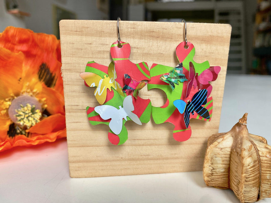 Beautiful, bright, multicoloured, puzzle shaped earrings with tiny butterflies, made from upcycled craft beer cans by Laura Zabo on a wooden background
