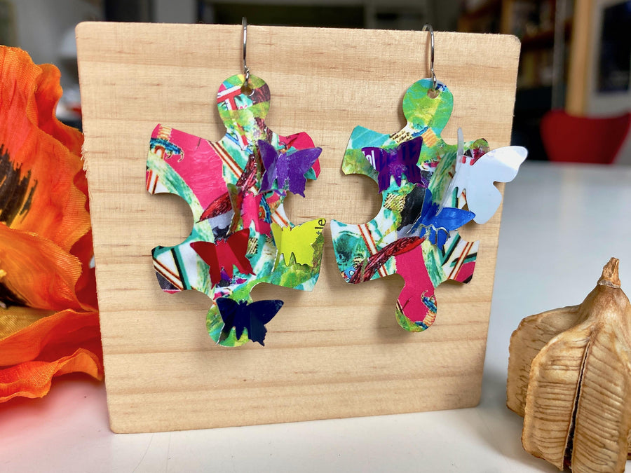 multicoloured, bright puzzle shaped earrings with butterflies made from craft beer cans by laura zabo on a wooden background and plant decoration