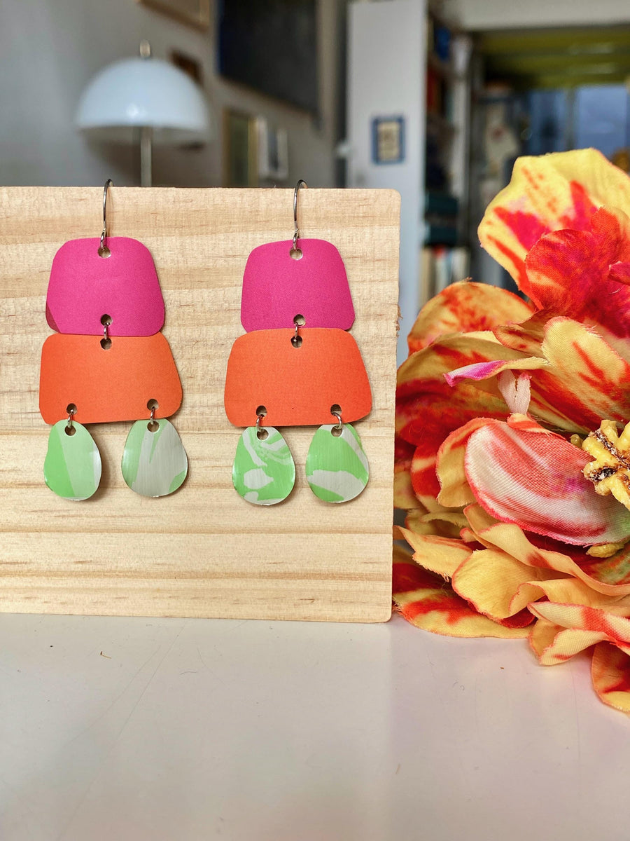 pink orange and green earrings made from upcycled craft beer cans and nespresso capsules by laura zabo on a wooden background and flower decoration