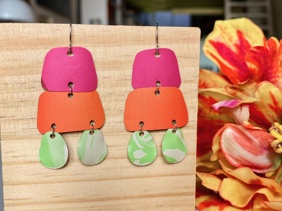 pink orange and green earrings made from upcycled craft beer cans and nespresso capsules by laura zabo on a wooden background and flower decoration