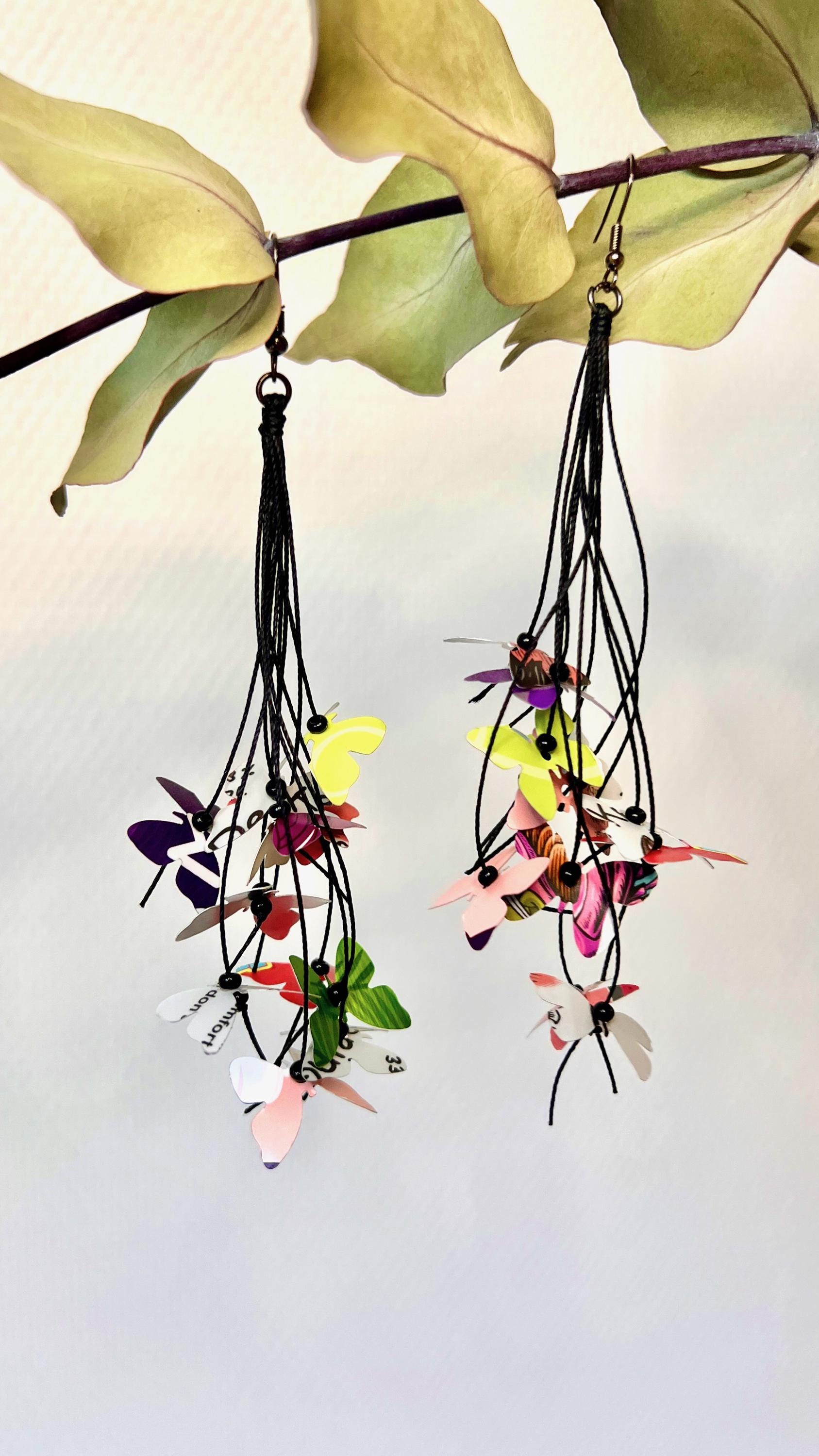 Upcycled earrings hanging on a dry wooden stick with leaves, the earrings feature tiny butterflies cut from soda and beer cans, fitted on waxed cotton cord