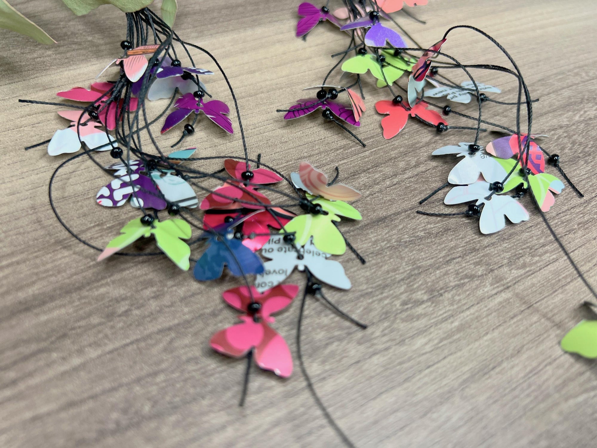 extra long, upcycled earrings hanging on a dry wooden stick with leaves, the earrings feature tiny butterflies cut from soda and beer cans, fitted on waxed cotton cord