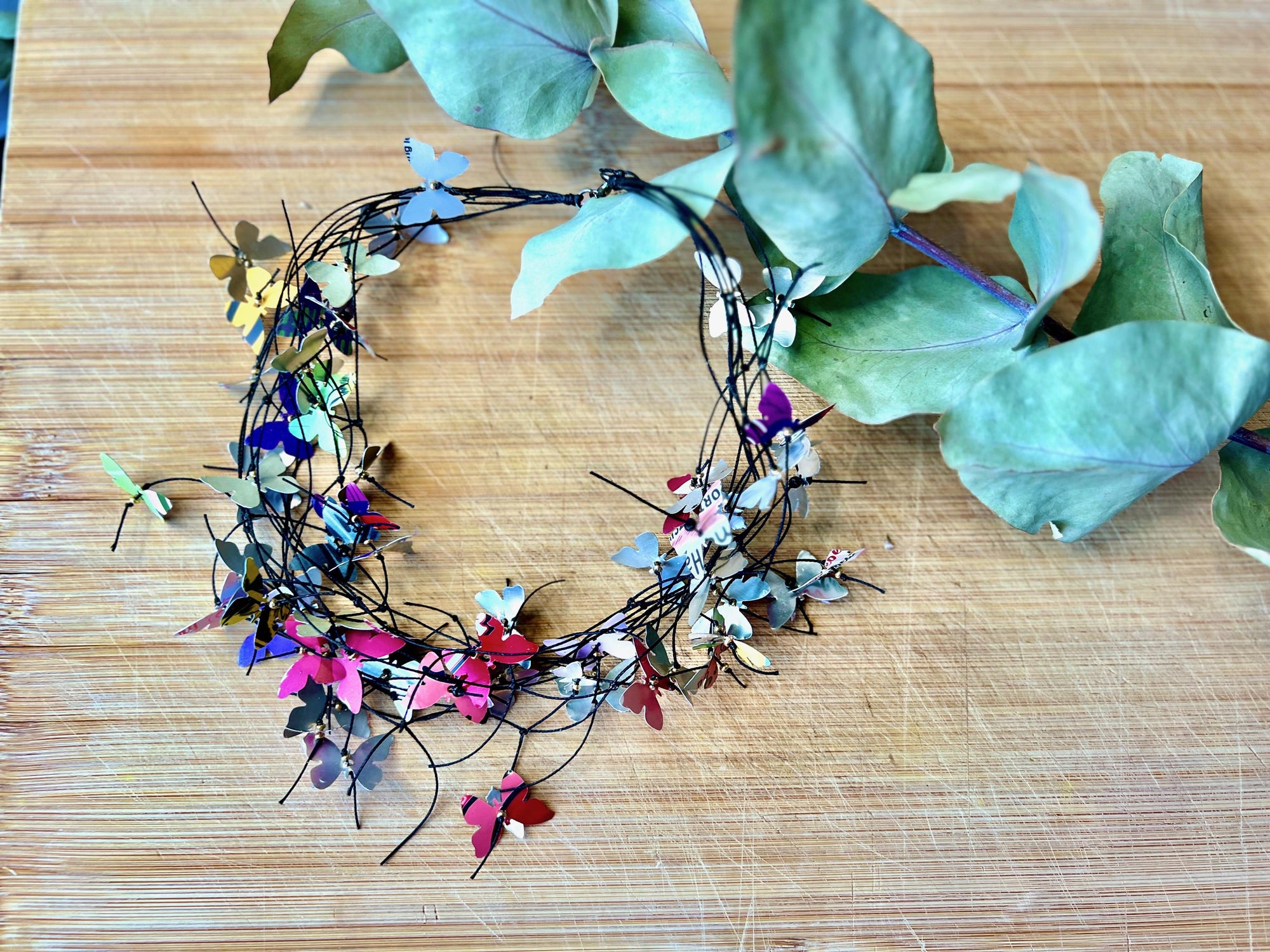 elegant, colourful necklace featuring tiny aluminium butterflies, each one is cut from soda and beer cans, fitted on multiple thin black waxed cotton cord on a wooden background