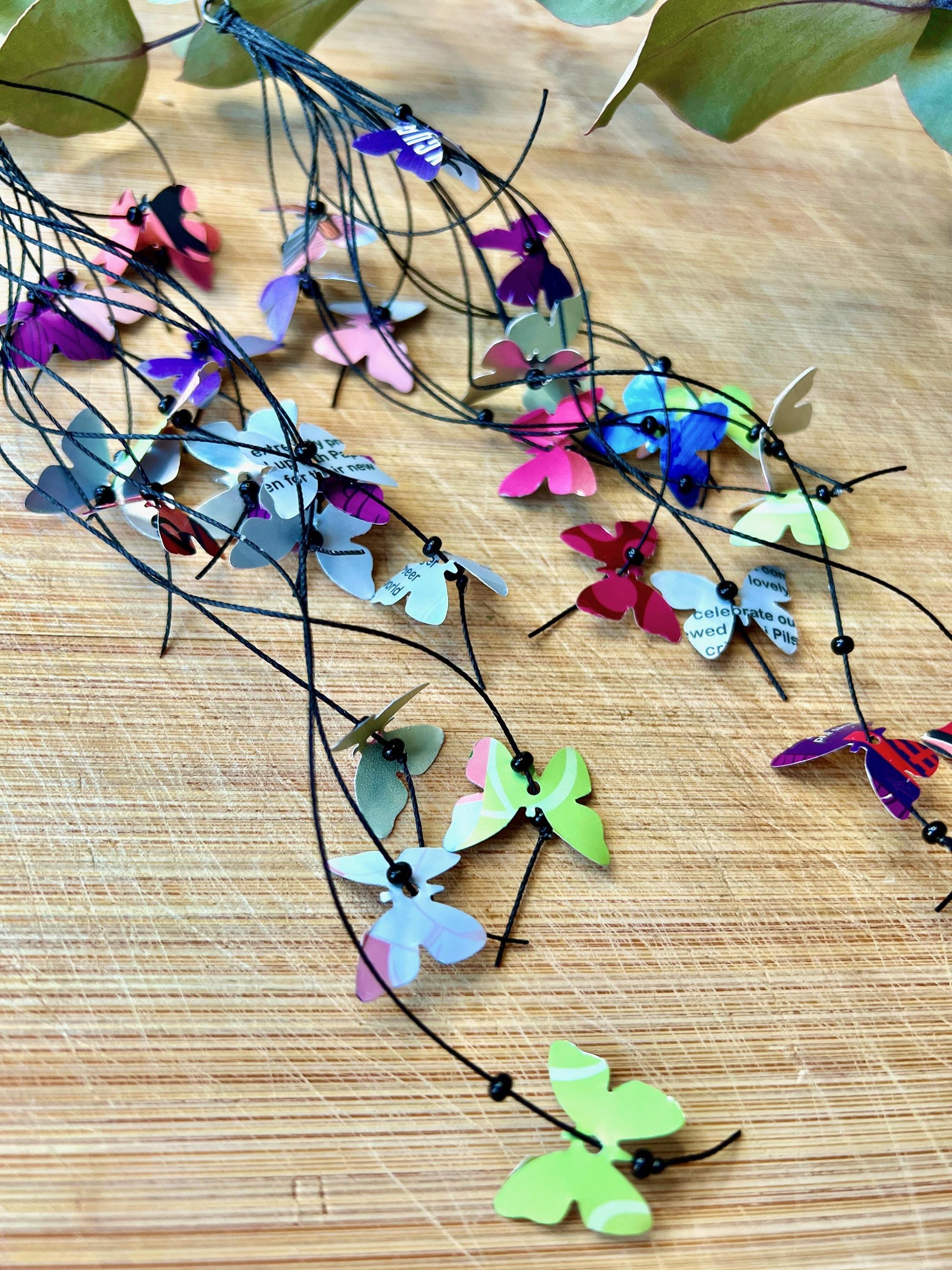 Extra long, Upcycled earrings on a wooden backround , the earrings feature tiny butterflies cut from soda and beer cans, fitted on waxed cotton cord