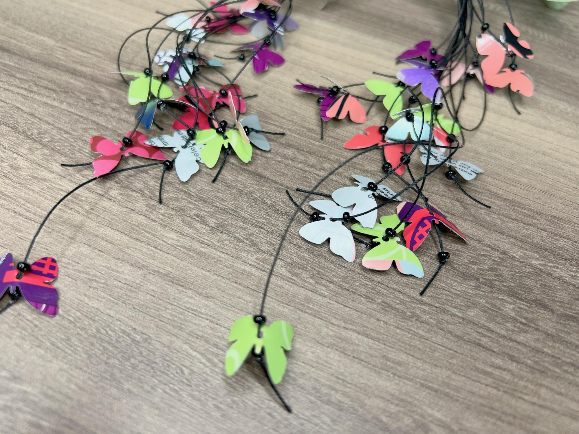 extra long, upcycled earrings hanging on a dry wooden stick with leaves, the earrings feature tiny butterflies cut from soda and beer cans, fitted on waxed cotton cord