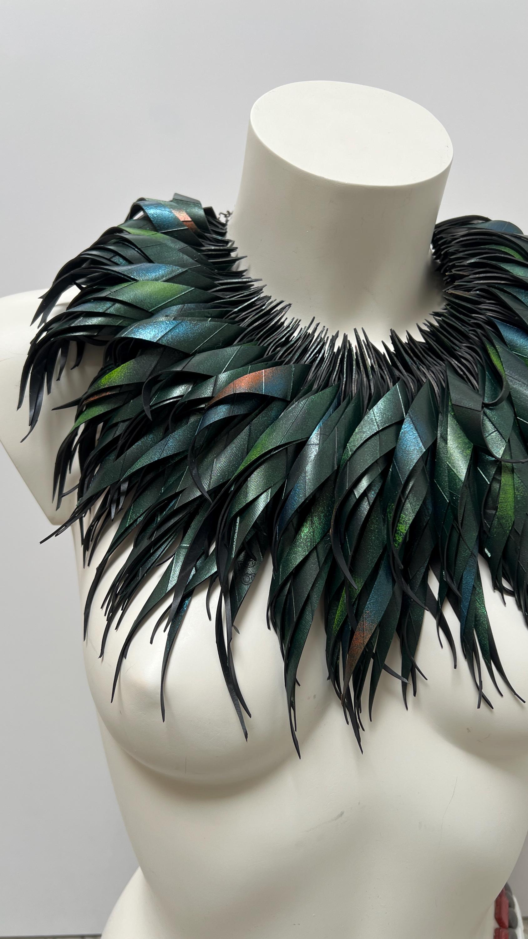 large, curly, dark green, jungle themed necklace made from upcycled bicycle inner tube rubber on a white mannequin, against a cosy room