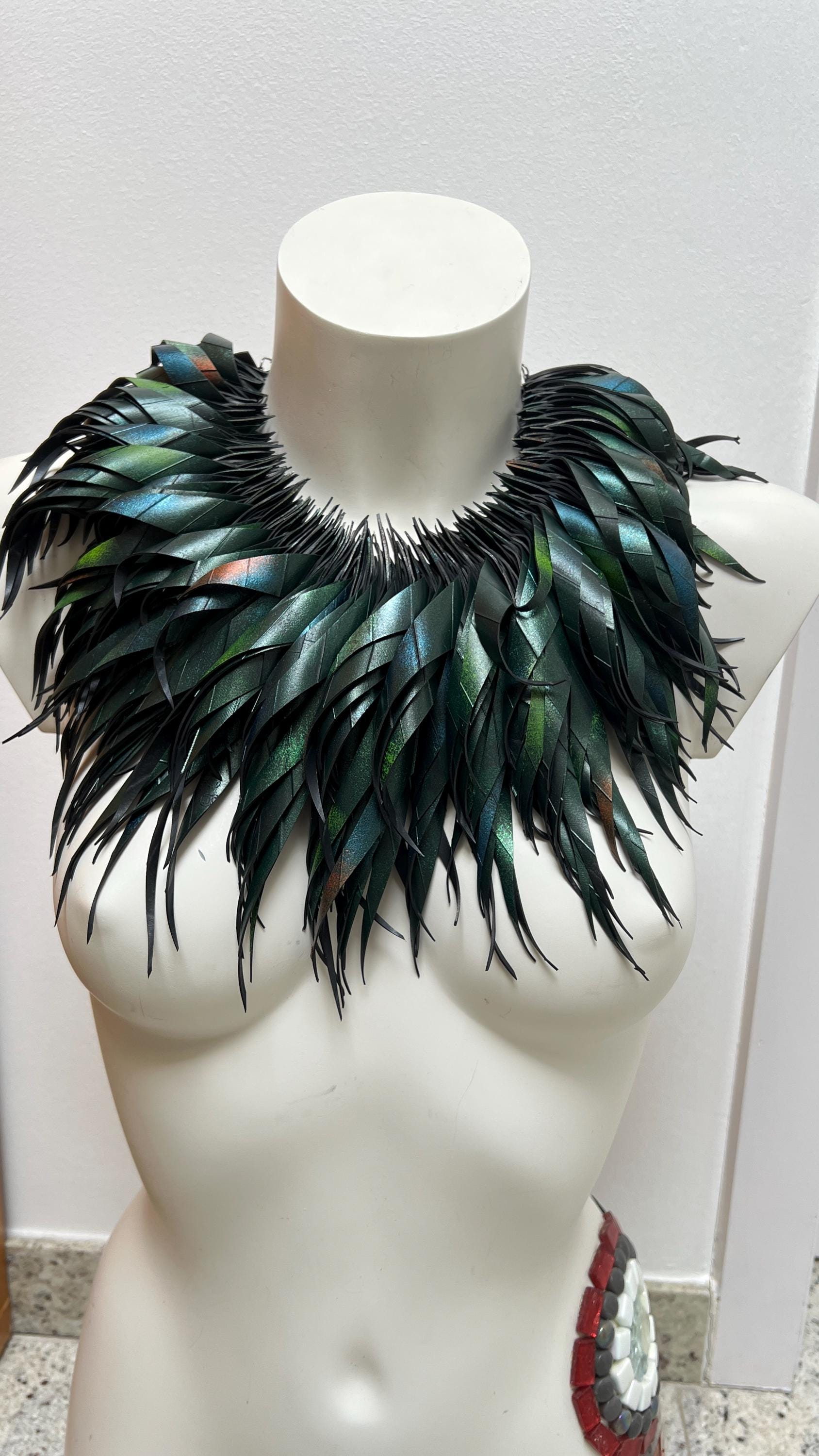 large, curly, dark green, jungle themed necklace made from upcycled bicycle inner tube rubber on a white mannequin, against a cosy room