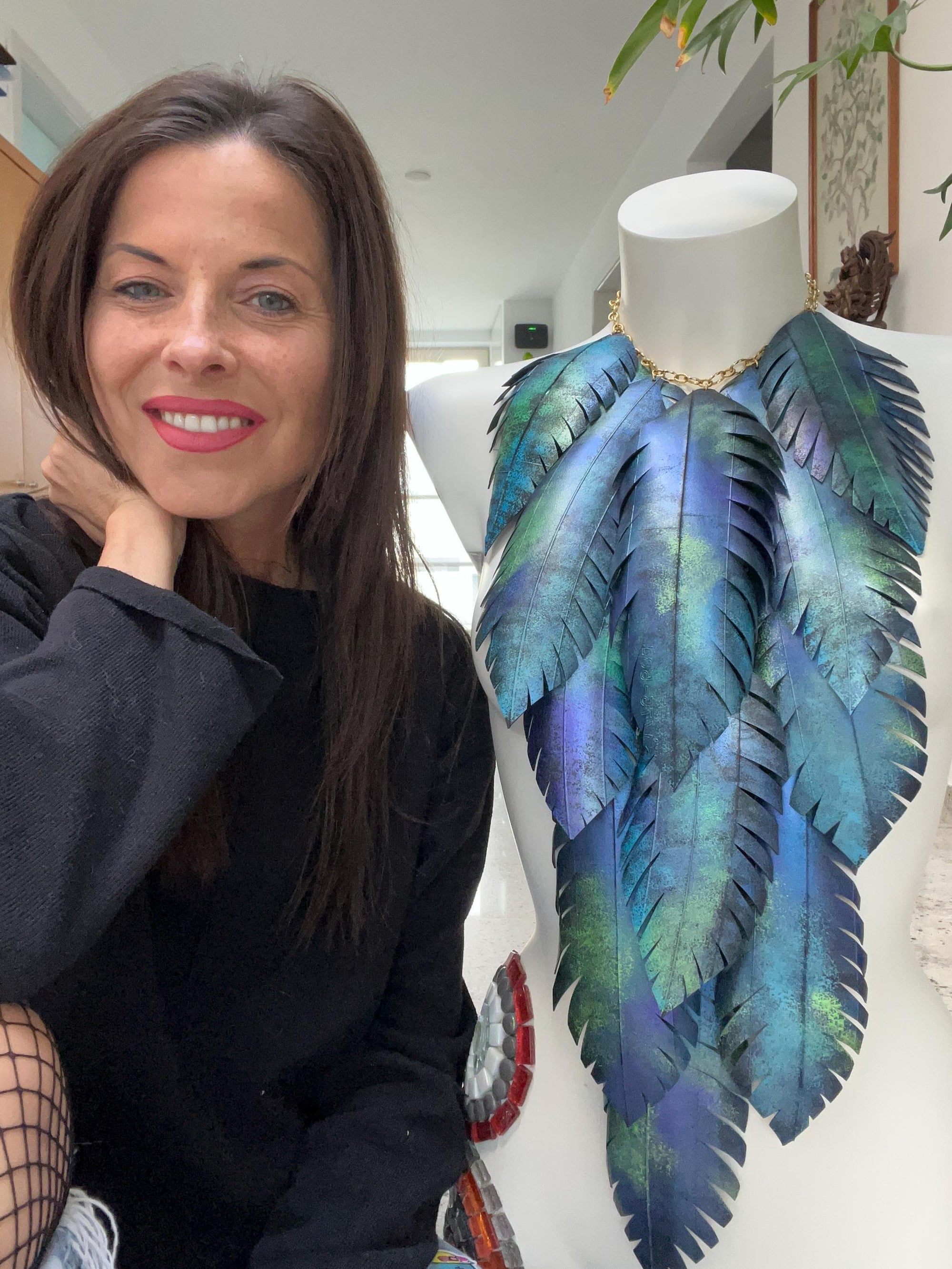 large blue green leaf necklace, neckpiece made from upcycled bicycle innertube rubber on a white mannequin and Laura Zabo sits next to the Mannequin