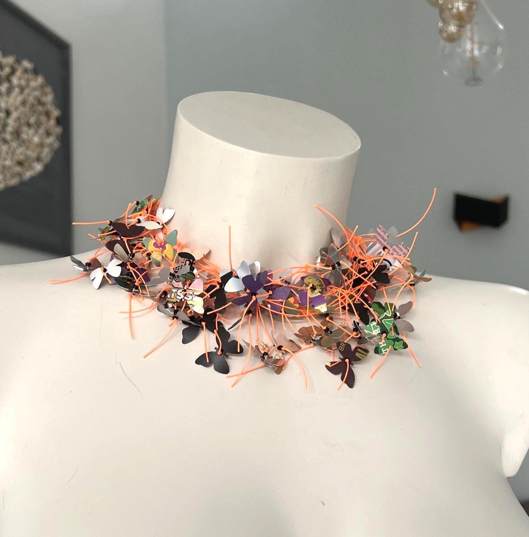 orange cord and aluminium butterfly necklace, the butterflies are cut from upcycled soda and beer cans on a white mannequin
