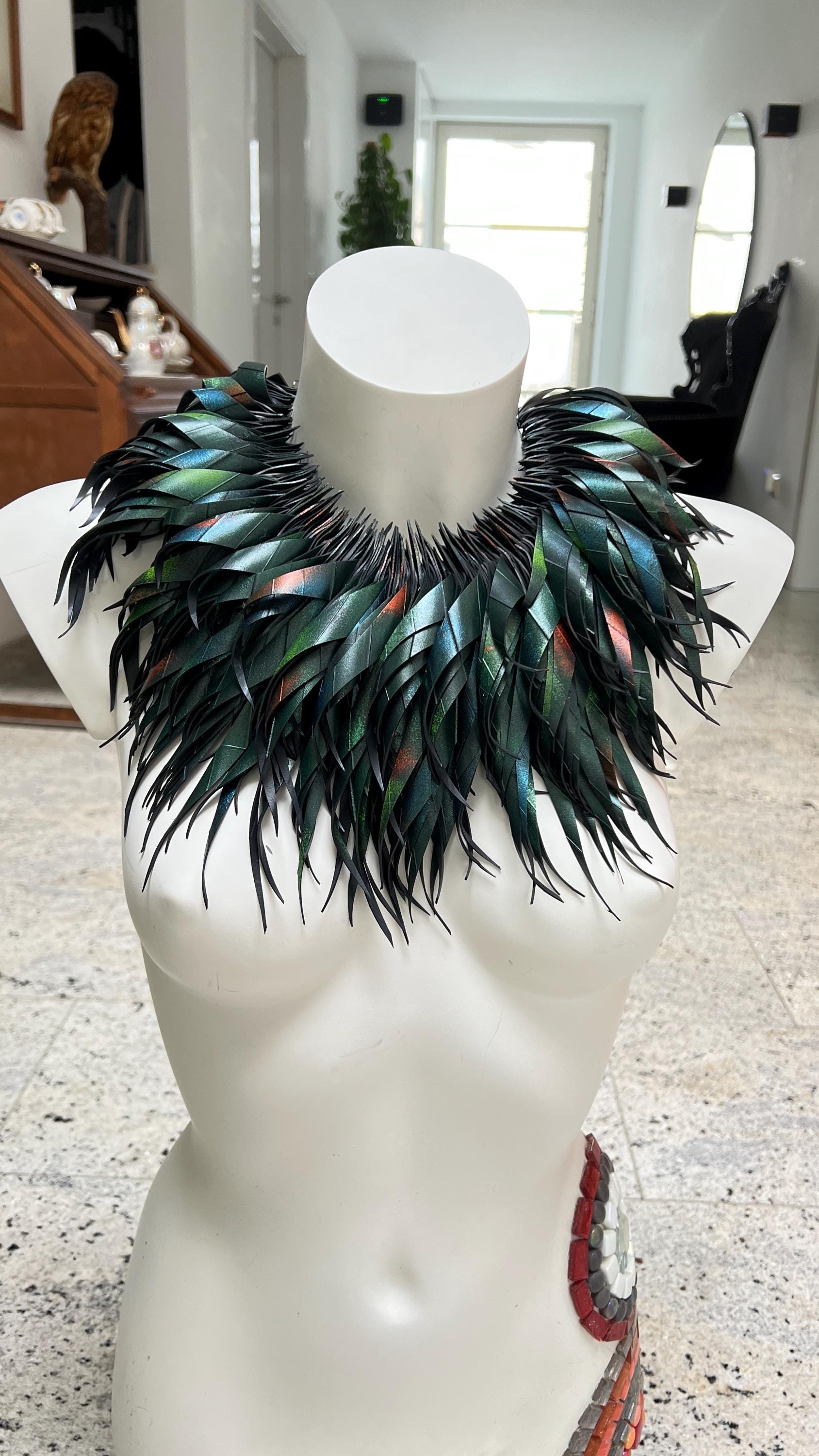 large, curly, dark green, jungle themed necklace made from upcycled bicycle inner tube rubber on a white mannequin, against a cosy room