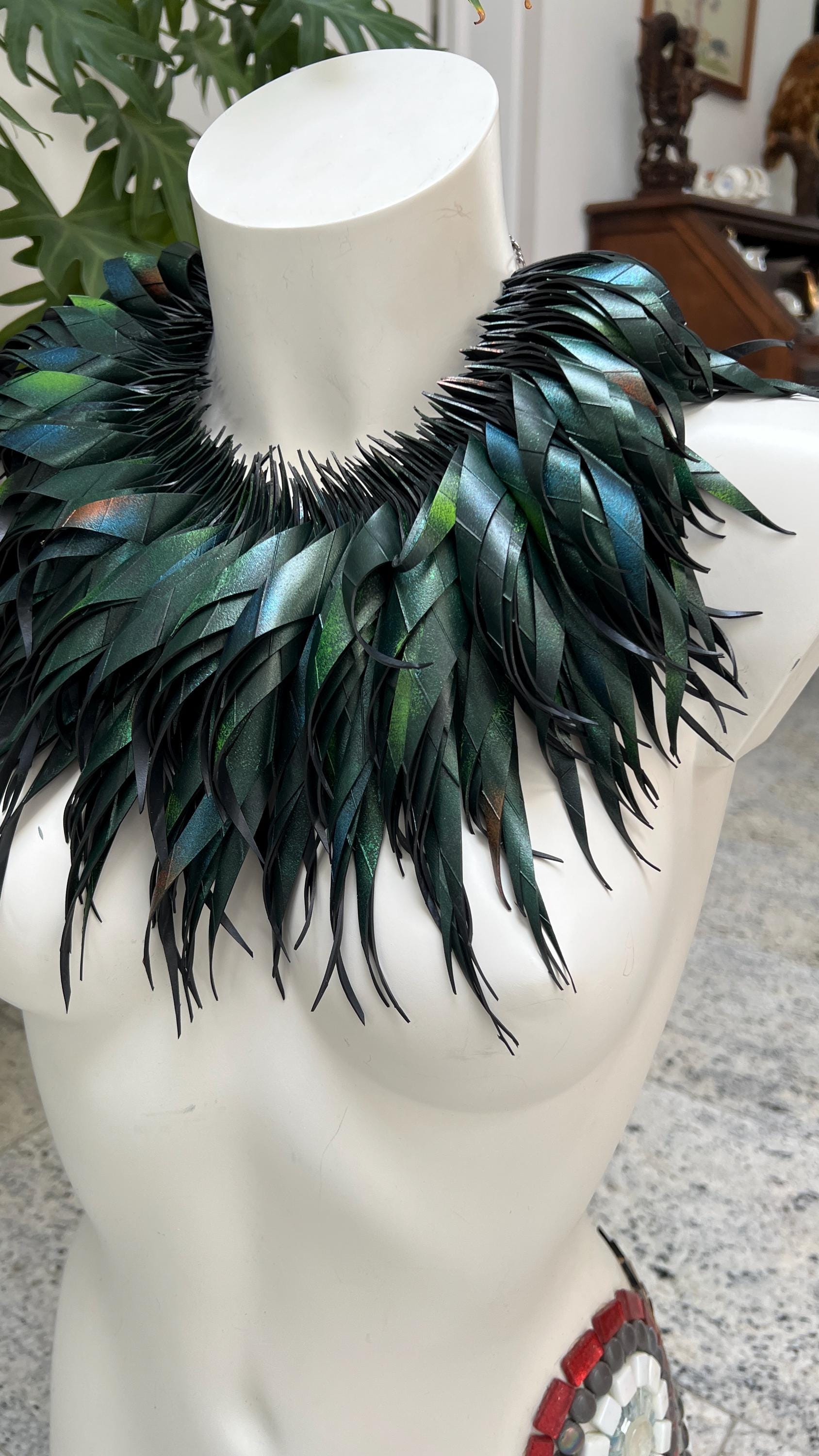 large, curly, dark green, jungle themed necklace made from upcycled bicycle inner tube rubber on a white mannequin, against a cosy room