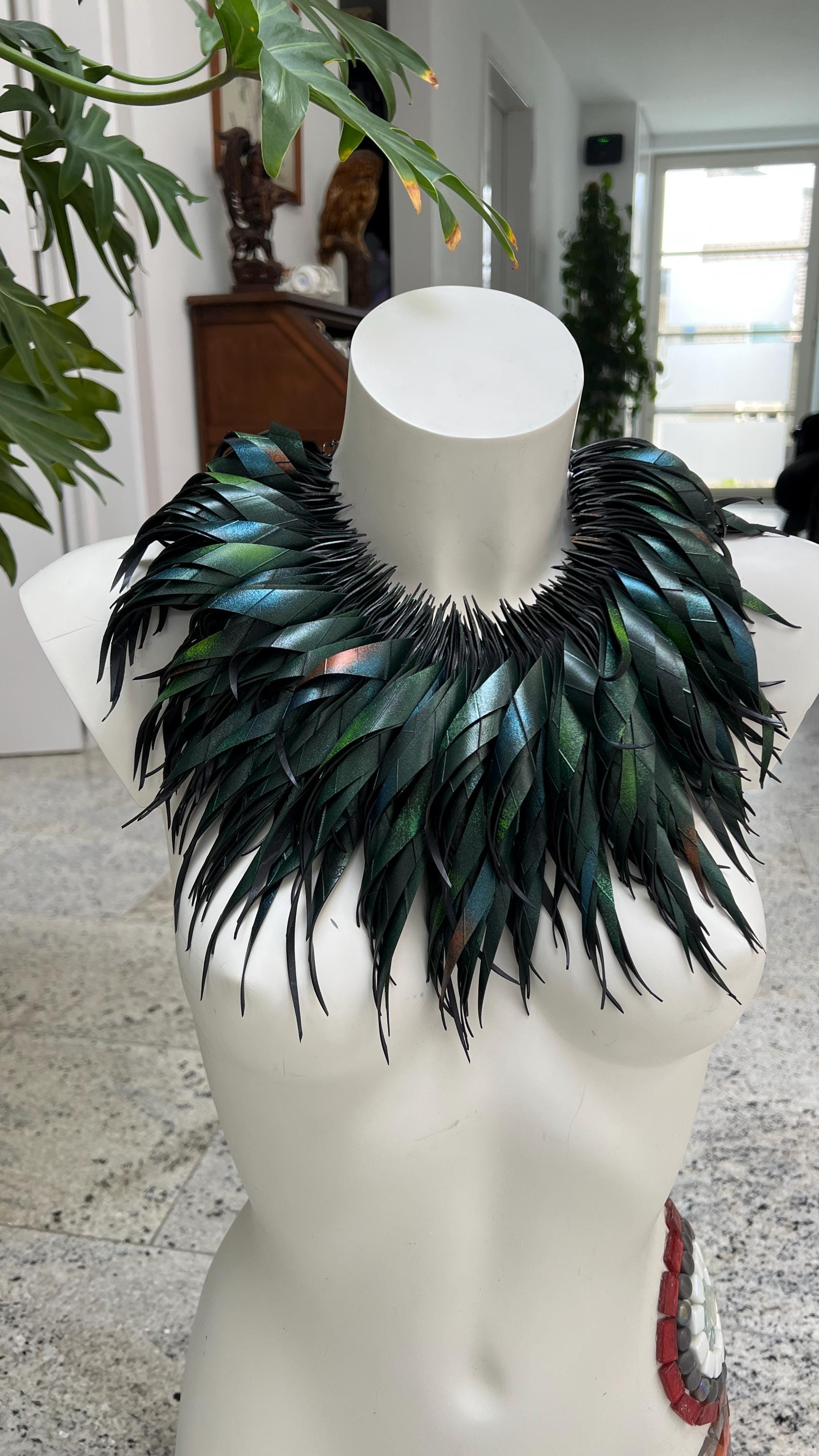 large, curly, dark green, jungle themed necklace made from upcycled bicycle inner tube rubber on a white mannequin, against a cosy room