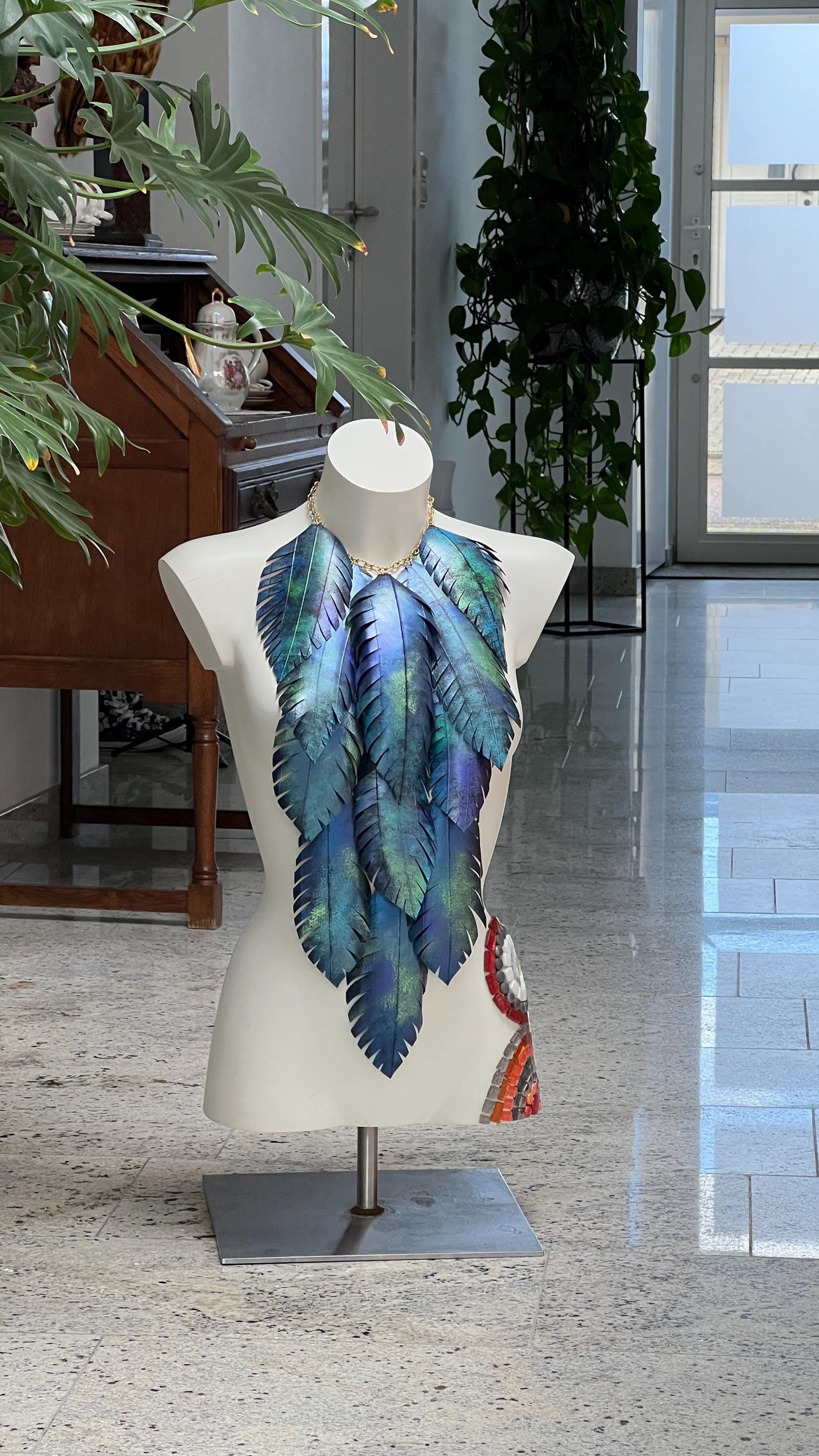 large blue green leaf necklace, neckpiece made from upcycled bicycle innertube rubber on a white mannequin against a cosy room