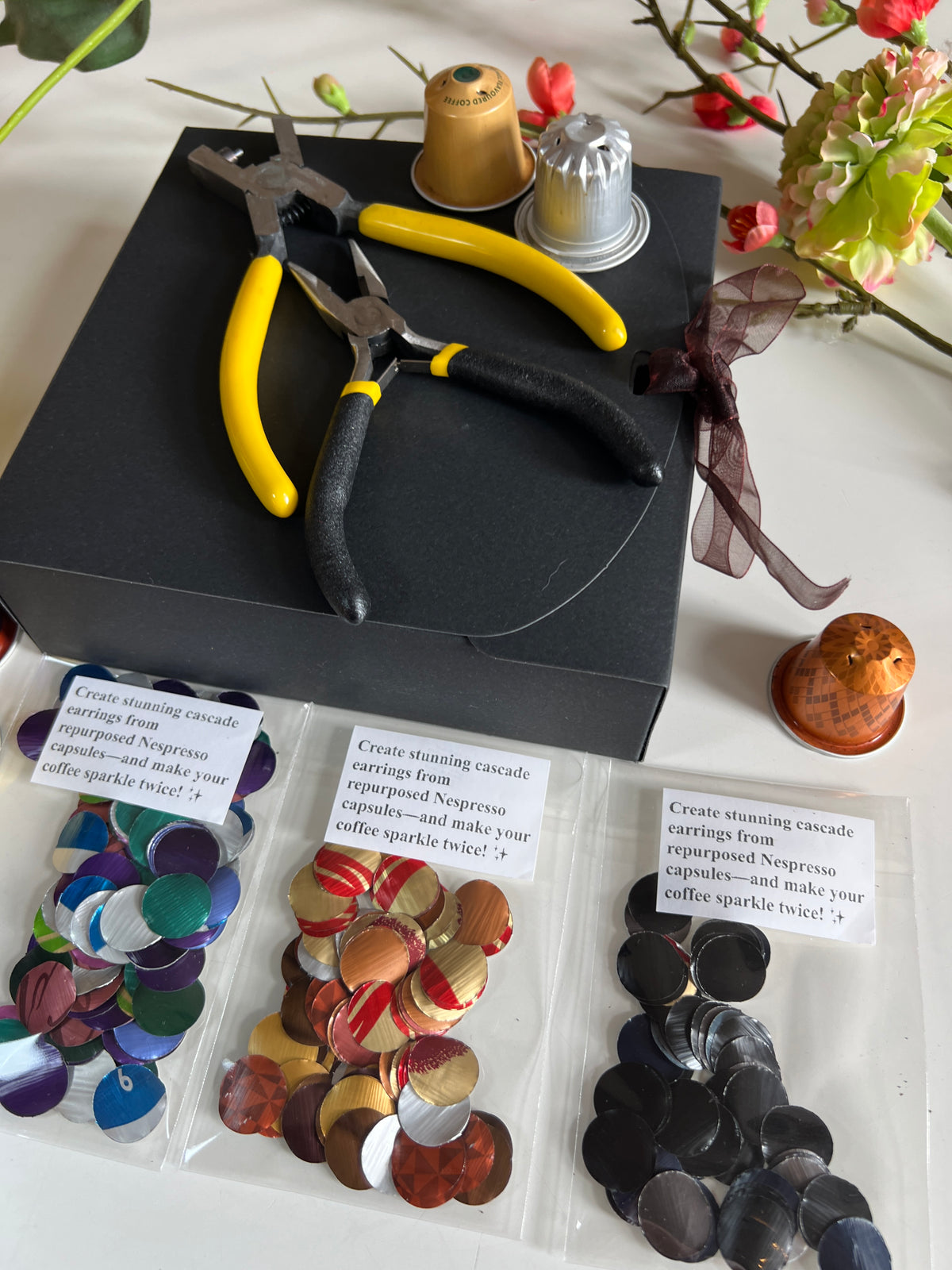 laura zabo beginner upcycling craft kit with aluminium circles cut from nespresso and coffee pods, craft pliers, black gift box, and some colourful nespresso capsules 