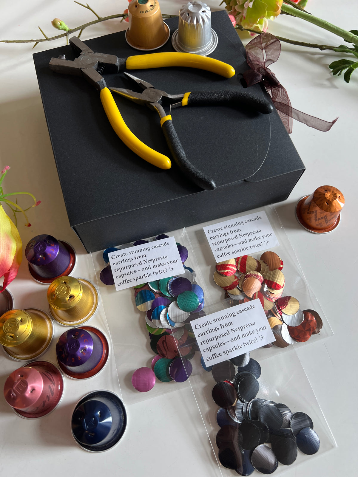 laura zabo beginner upcycling craft kit with aluminium circles cut from nespresso and coffee pods, craft pliers, black gift box, and some colourful nespresso capsules 