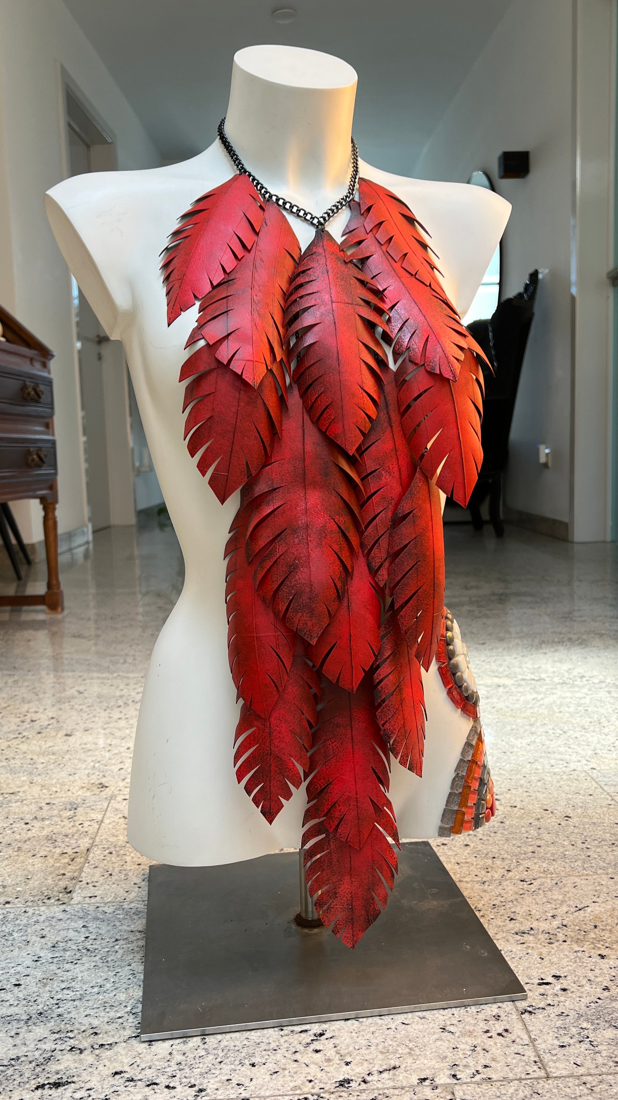 very large, red coloured, layered leaf shaped statement necklace made from upcycled bike tyre rubber on a white mannequin in a home environment