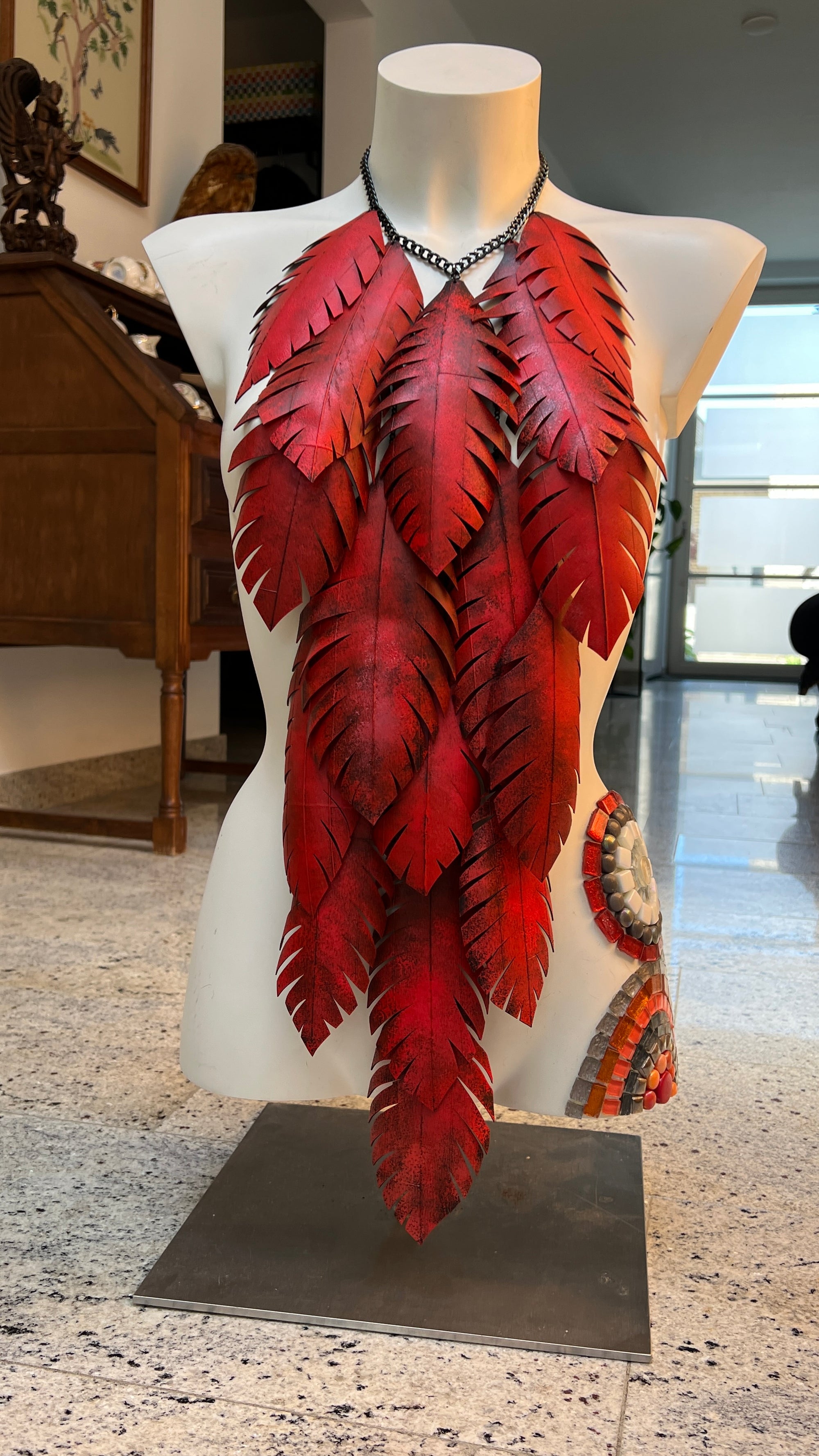 very large, red coloured, layered leaf shaped statement necklace made from upcycled bike tyre rubber on a white mannequin in a home environment